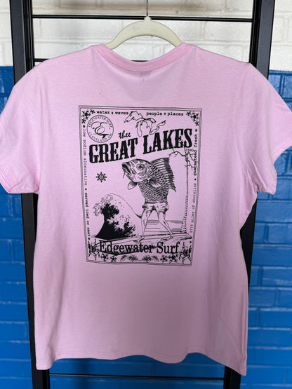 Pink t-shirt with 'Great Lakes' graphic design on a hanger against a blue brick wall.