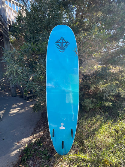 Blue surfboard on a grassy area with trees in the background