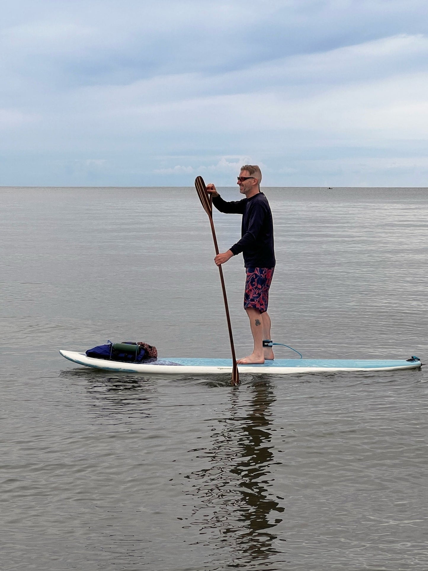 Person paddleboarding on a calm body of water with a clear sky.