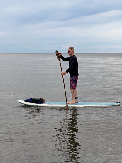 Person paddleboarding on a calm body of water with a clear sky.