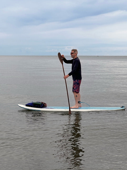 Person paddleboarding on a calm body of water with a clear sky.