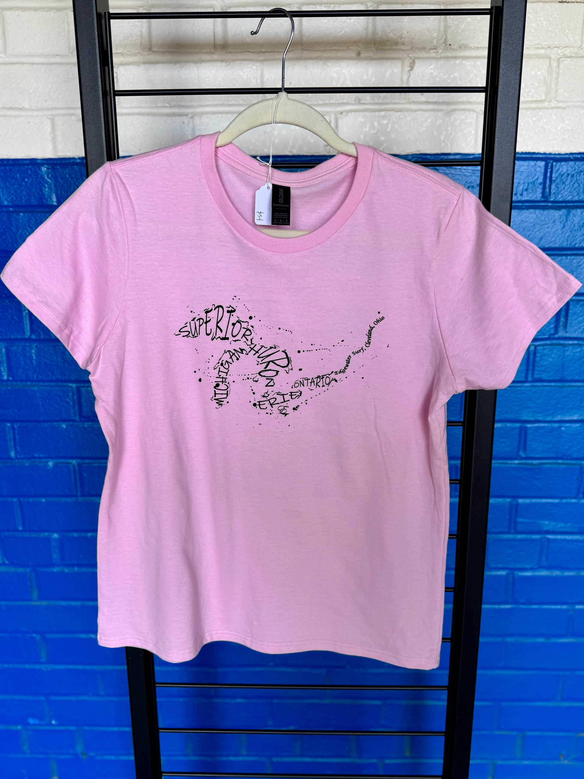 Pink t-shirt with black graphics on a hanger against a blue brick wall.